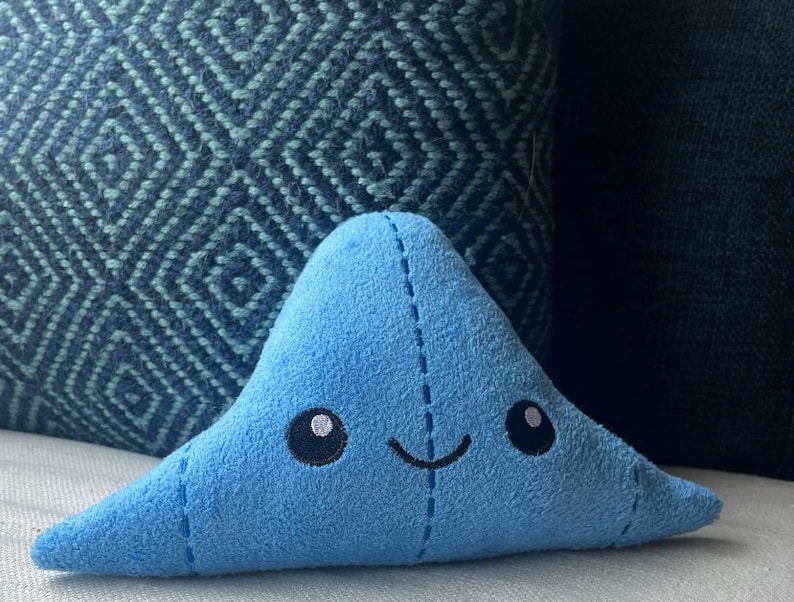 May include: A blue plush toy shaped like a triangle with a smiling face and stitched details.