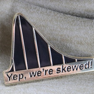 May include: A black and gold metal pin shaped like a roller coaster with the text "Yep, we're skewed!"