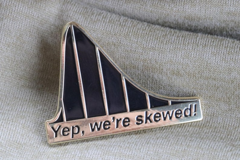May include: A black and gold metal pin shaped like a roller coaster with the text "Yep, we're skewed!"