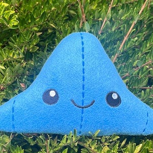 May include: A blue plush toy shaped like a blob with a smiling face and embroidered eyes.