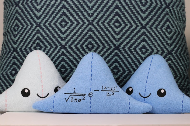 May include: Three blue and white plush pillows shaped like triangles. The middle pillow has a mathematical formula embroidered on it: "1/&radic;2&pi;&sigma;&sup2; e^-(x-&mu;)&sup2;/2&sigma;&sup2;".