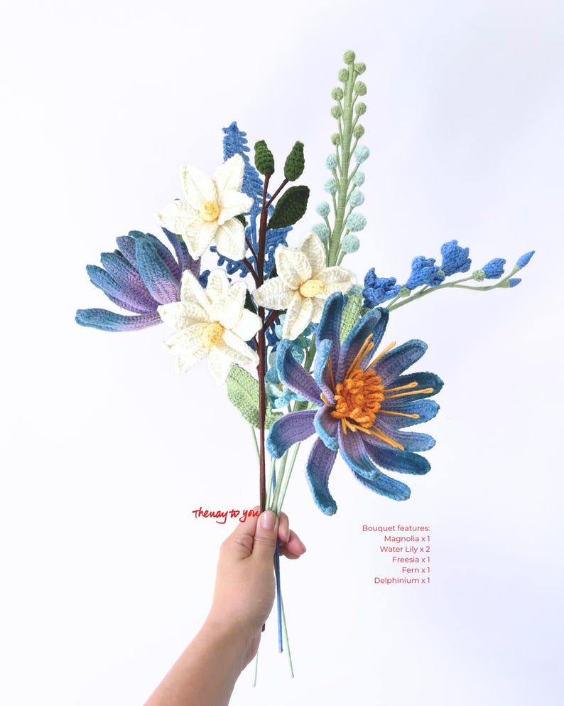 May include: A crocheted bouquet of flowers in shades of blue, white, and green. The bouquet includes a magnolia, two water lilies, a freesia, a fern, and a delphinium. The text "Thenay to you" is written on the stems.