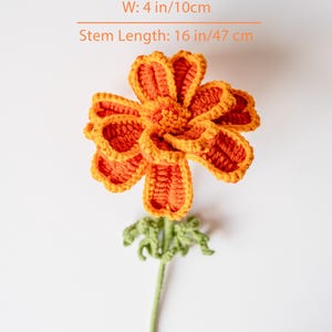 May include: A handmade crochet flower in shades of orange and yellow, with a green stem and leaves. The flower is 4 inches wide and the stem is 16 inches long. The text on the image reads: W: 4 in/10cm, Stem Length: 16 in/47 cm.