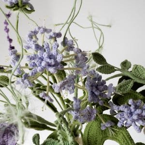 May include: A crocheted bouquet of purple and green flowers. The flowers are made of yarn and have a realistic appearance.