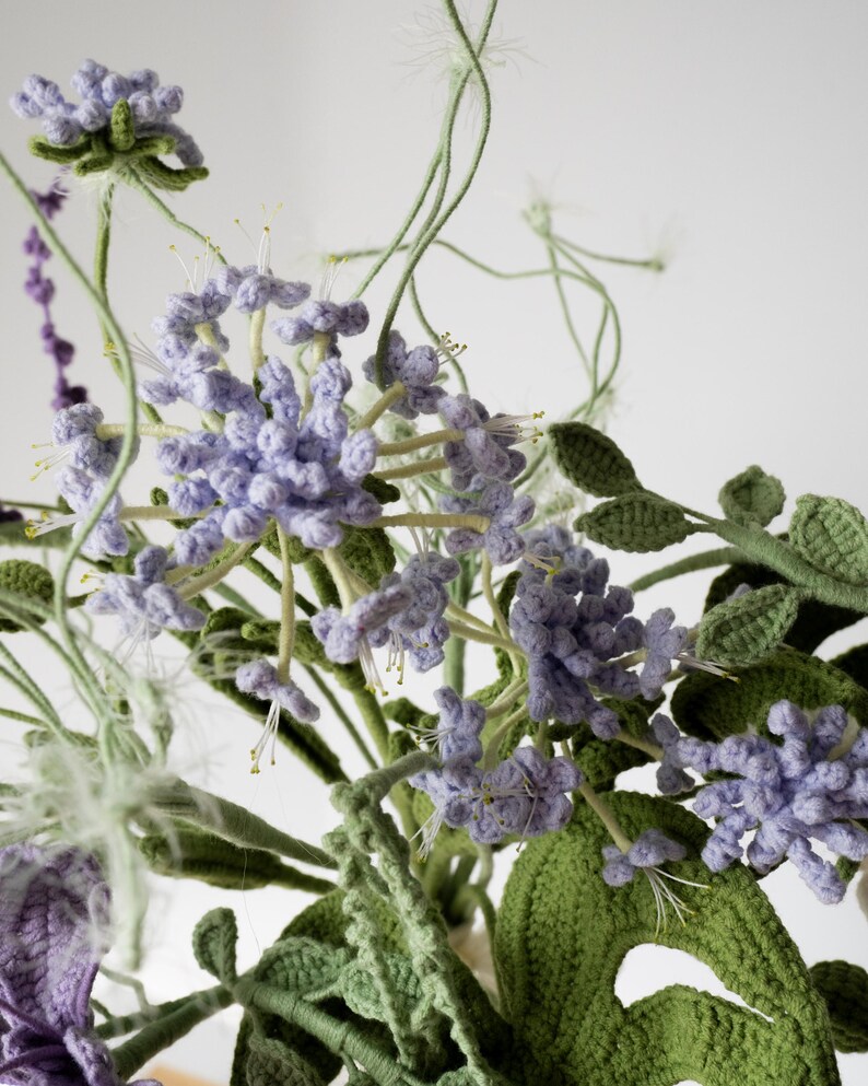 May include: A crocheted bouquet of purple and green flowers. The flowers are made of yarn and have a realistic appearance.