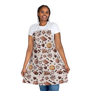 May include: A beige apron with a pattern of chocolate bars, cakes, cookies, and hearts. The apron is being worn by a person with dark brown hair.