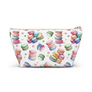 May include: A white zippered pouch featuring a repeating watercolor print of colorful French macarons in shades of pink, blue, green, yellow, and orange, interspersed with small scattered polka dots in various pastel colors across the entire surface.