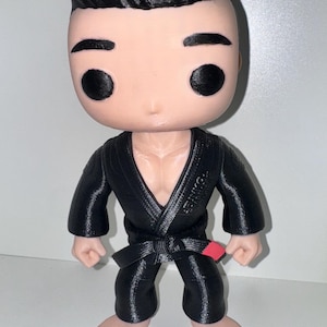 May include: A Funko Pop figure of a martial artist in a black gi with a red belt. The figure has a light skin tone, black hair, and black eyes. The gi has the word "YONKE" printed on the chest.