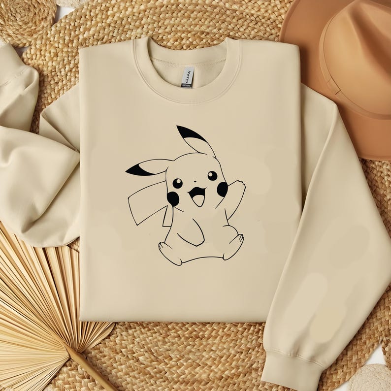 May include: A beige sweatshirt with a black outline of Pikachu, a popular cartoon character, on the front.