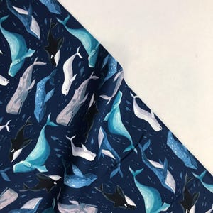 Pode incluir: Um tecido azul marinho com um padrão repetido de baleias em vários tons de azul, branco e preto. As baleias nadam em direções diferentes e algumas estão parcialmente obscurecidas por outras baleias.