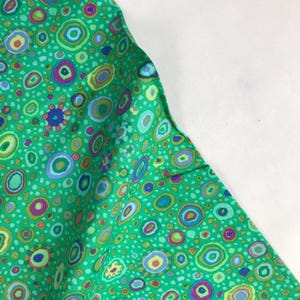 以下が含まれることがあります： カラフルな円と点の繰り返しパターンが施された緑色の生地です。