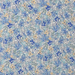 May include: A fabric with a floral pattern. The design features small blue, light blue, yellow, and white flowers on a gray background. The flowers are densely packed, creating a textured appearance.