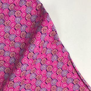 May include: Purple fabric with a repeating pattern of pink, white, and orange concentric circles.
