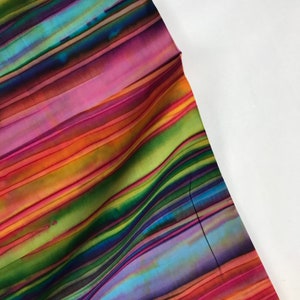 Könnte beinhalten: Ein lebendiger Stoff mit diagonalen Streifen in einem Farbspektrum, darunter Rosa, Orange, Grün, Blau und Lila. Der Stoff hat eine fließende, wellenförmige Textur, mit einem weißen Hintergrund auf der rechten Seite des Bildes. Der Gesamteffekt ist farbenfroh und dynamisch.