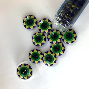 May include: A container of assorted buttons with a green, yellow, and purple sun design. The buttons are in a clear plastic container with a white background.