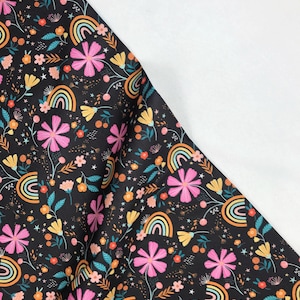 May include: Black fabric with a colorful floral and rainbow pattern. The design features pink flowers, yellow flowers, and small orange flowers, with teal leaves and small white stars. The rainbows have orange, yellow, and green stripes.
