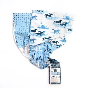 May include: A length of fabric featuring a white background with a repeating pattern of dark blue and light blue running horses, desert landscapes, and cacti. The fabric includes a selvage edge with small icons and a label reading Desert Horses.