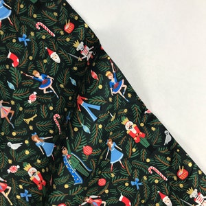 May include: Black fabric with a festive Christmas pattern. The design features illustrations of nutcrackers, ballerinas, candy canes, and Christmas ornaments. The background is filled with green pine needles and gold accents, creating a holiday theme.