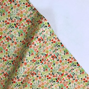 Może przedstawiać: Zbliżenie na tkaninę w kwiaty z gęstym wzorem małych kwiatów w odcieniach czerwieni, różu, zieleni i żółci na kremowym tle. Tkanina jest złożona, odsłaniając białą powierzchnię.