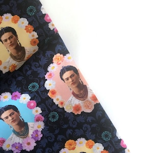 May include: Black fabric with a repeating pattern of Frida Kahlo's portrait surrounded by colorful flowers. The background is a dark blue with a floral pattern.