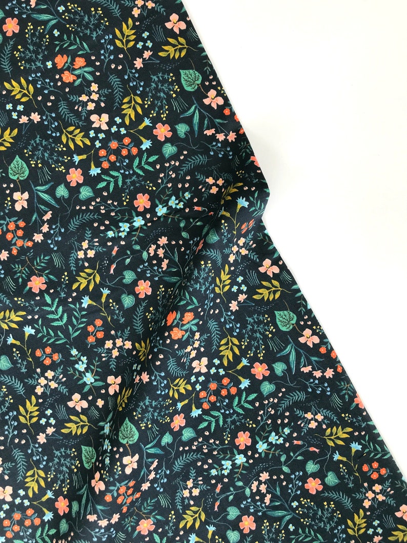 Peut inclure: Tissu bleu marine fonc&eacute; avec un motif floral color&eacute;. Le motif pr&eacute;sente de petites fleurs p&ecirc;che, bleues et blanches, ainsi que des feuilles et des tiges vertes et jaunes. Le tissu est pli&eacute;, montrant l'impression d&eacute;taill&eacute;e.