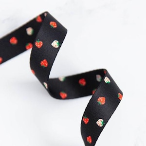 Peut inclure: Ruban noir orné d'un motif répété de fraises rouges et blanches avec des feuilles vertes. Le ruban est enroulé, suggérant une utilisation pour l'artisanat ou l'emballage cadeau.