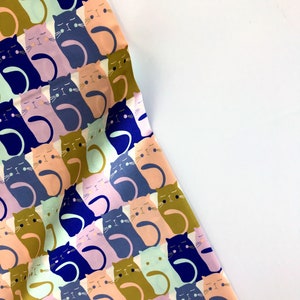 May include: A white fabric with a repeating pattern of colorful cats. The cats are in various shades of pink, blue, green, and brown. They are all facing forward with their eyes closed and their tails curled around their bodies.