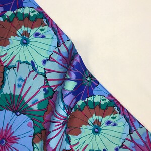May include: A blue and green fabric with a floral pattern of large, stylized flowers. The flowers have a blue, green, and brown color scheme.