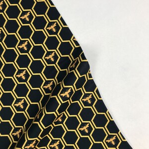 Könnte beinhalten: Schwarzer Stoff mit einem sich wiederholenden Muster aus gelben Wabenformen und goldenen Bienen.