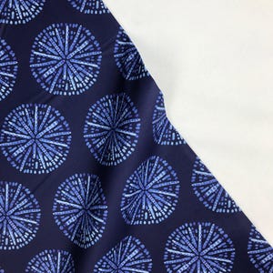 May include: Navy blue fabric with a repeating pattern of blue and white stylized starbursts. The fabric is folded in half, with the white side of the fold visible.