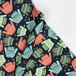 May include: A navy blue fabric with a repeating pattern of colourful Christmas jumpers. The jumpers are in shades of green, red, and blue with white accents. Gold stars are scattered throughout the fabric.