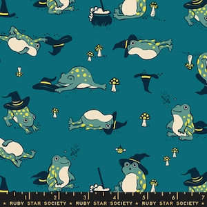 May include: A teal fabric featuring a repeating pattern of green frogs with yellow spots, some wearing black pointed hats. The design includes small white mushrooms, black cauldrons, and tiny stars. A black selvage edge displays the text RUBY STAR SOCIETY.