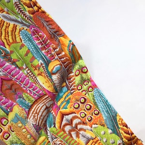 May include: A colorful fabric with a pattern of feathers in shades of orange, yellow, green, blue, pink, and brown. The feathers are arranged in a random pattern and overlap each other.