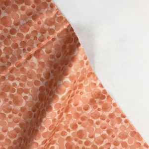 May include: A close-up of a peach-colored fabric with a white background and a pattern of orange circles.