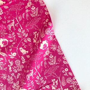 May include: Pink fabric with a white floral and animal print. The print features deer, birds, and other woodland creatures.