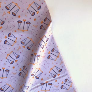 Puede incluir: Tela morada con un patrón repetido de escamas doradas y la palabra "Libra" en rosa.