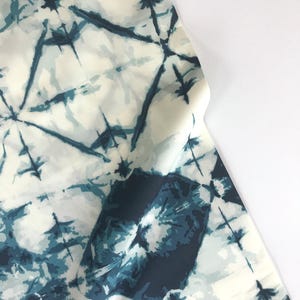 May include: White fabric with a blue tie-dye pattern. The pattern features a series of abstract shapes and lines.