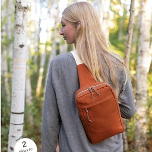 May include: A brown sling bag with a zipper closure and a strap. The bag is being worn by a person in a gray sweatshirt and blue jeans. The text "SANDHILL" and "a compact hands-free sling style bag" is above the image. The text "2 views to sew!" is in a circle on the left side of the image. The text "noodlehead" is at the bottom of the image.