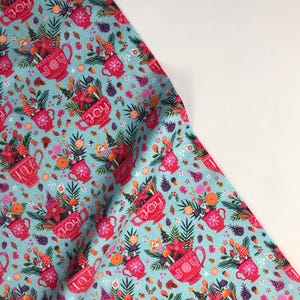 May include: A blue fabric with a repeating pattern of red mugs filled with Christmas-themed items and the word "JOY" on the mugs. The mugs are surrounded by a variety of festive elements, including pine branches, holly, cinnamon sticks, and baubles.