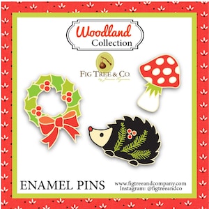 May include: Three enamel pins featuring a red and green holly wreath with a red bow, a black and white hedgehog with green pine needles, and a red and white mushroom with green stems. The pins are part of the Woodland Collection by Fig Tree & Co.