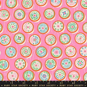 May include: Pink fabric with a repeating pattern of colorful thread spools. Each spool has a cream-colored center with a different design and text, surrounded by an orange ring. The spools are connected by white thread lines. The text "Ruby Star Society" is at the bottom.