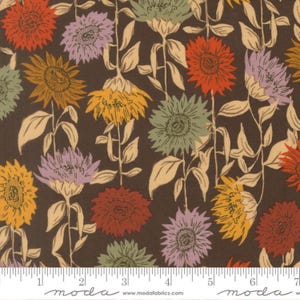 May include: A dark brown fabric featuring a repeating pattern of sunflowers in shades of red, yellow, lavender, and sage green. The sunflowers have long stems and leaves, and a white ruler is visible at the bottom with the text moda fabrics.