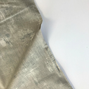 Może przedstawiać: Zbliżenie beżowego materiału z abstrakcyjnym wzorem w jasnozielonym i białym kolorze. Materiał ma fakturowaną, szczotkowaną powierzchnię.