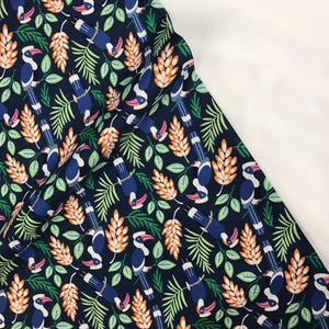 May include: A dark blue fabric with a repeating pattern of white and blue toucans, orange and green leaves, and white and orange flowers.