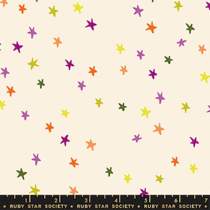 May include: A cream-colored fabric featuring a scattered pattern of hand-drawn stars in shades of orange, purple, lime green, and olive green. A black ruler at the bottom shows measurements in inches, with the text Ruby Star Society printed repeatedly.