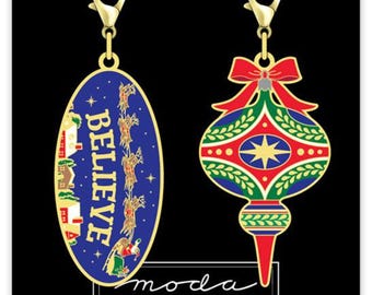 May include: Two gold-tone Christmas ornament charms. One charm is a blue oval with the word "BELIEVE" in gold lettering and a scene of Santa's sleigh flying through the night sky. The other charm is a red, green, and gold ornament with a star in the center.