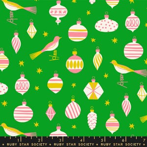 May include: A green fabric featuring a repeating pattern of pink and white Christmas ornaments in various shapes, yellow birds perched on springs, and small yellow stars. A black ruler with the text Ruby Star Society is visible at the bottom.