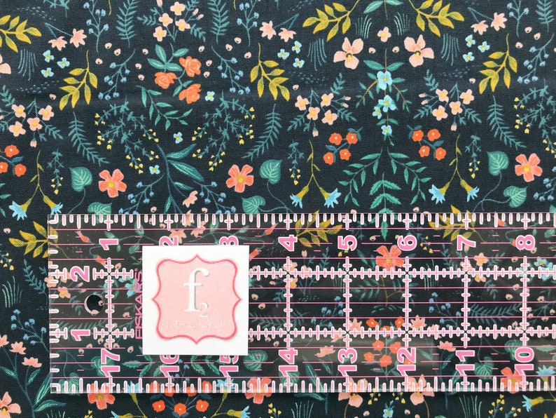 Peut inclure: Tissu bleu marine fonc&eacute; avec un motif floral compos&eacute; de fleurs et de feuillages orange, roses, jaunes et turquoise. Une r&egrave;gle transparente avec des marquages roses et une &eacute;tiquette blanche avec un bord rose et la lettre "f".
