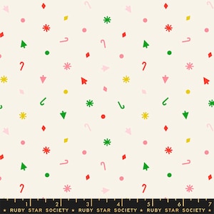 May include: A cream-colored fabric featuring a repeating pattern of small, colorful holiday-themed icons including red candy canes, green pine trees, yellow and pink stars, and various geometric shapes. A black ruler is visible at the bottom.