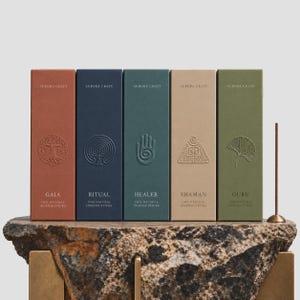 Può includere: Cinque scatole rettangolari di incenso Aurora Craft con icone e nomi in rilievo: Gaia in terracotta, Ritual in blu navy, Healer in verde ottanio, Shaman in beige e Guru in verde oliva. Un bastoncino di incenso è inserito in un supporto in ottone.